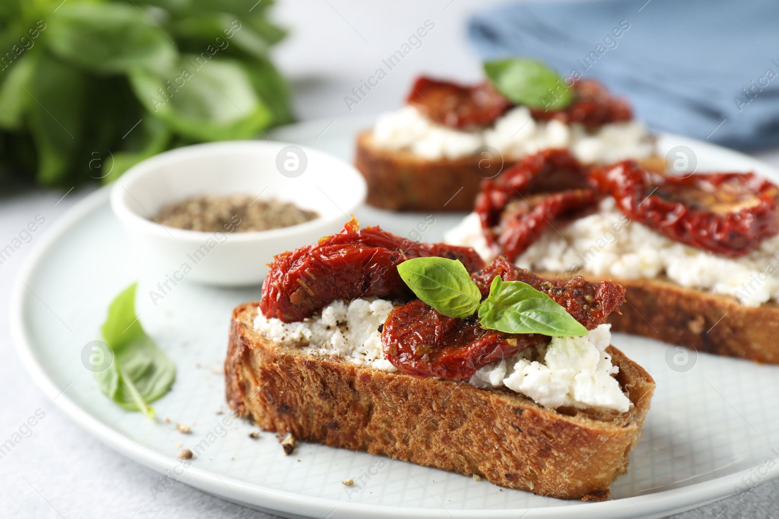 Photo of Delicious ricotta bruschettas with sun dried tomatoes, basil and milled pepper on light table, closeup