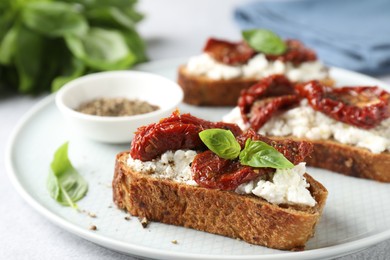 Delicious ricotta bruschettas with sun dried tomatoes, basil and milled pepper on light table, closeup