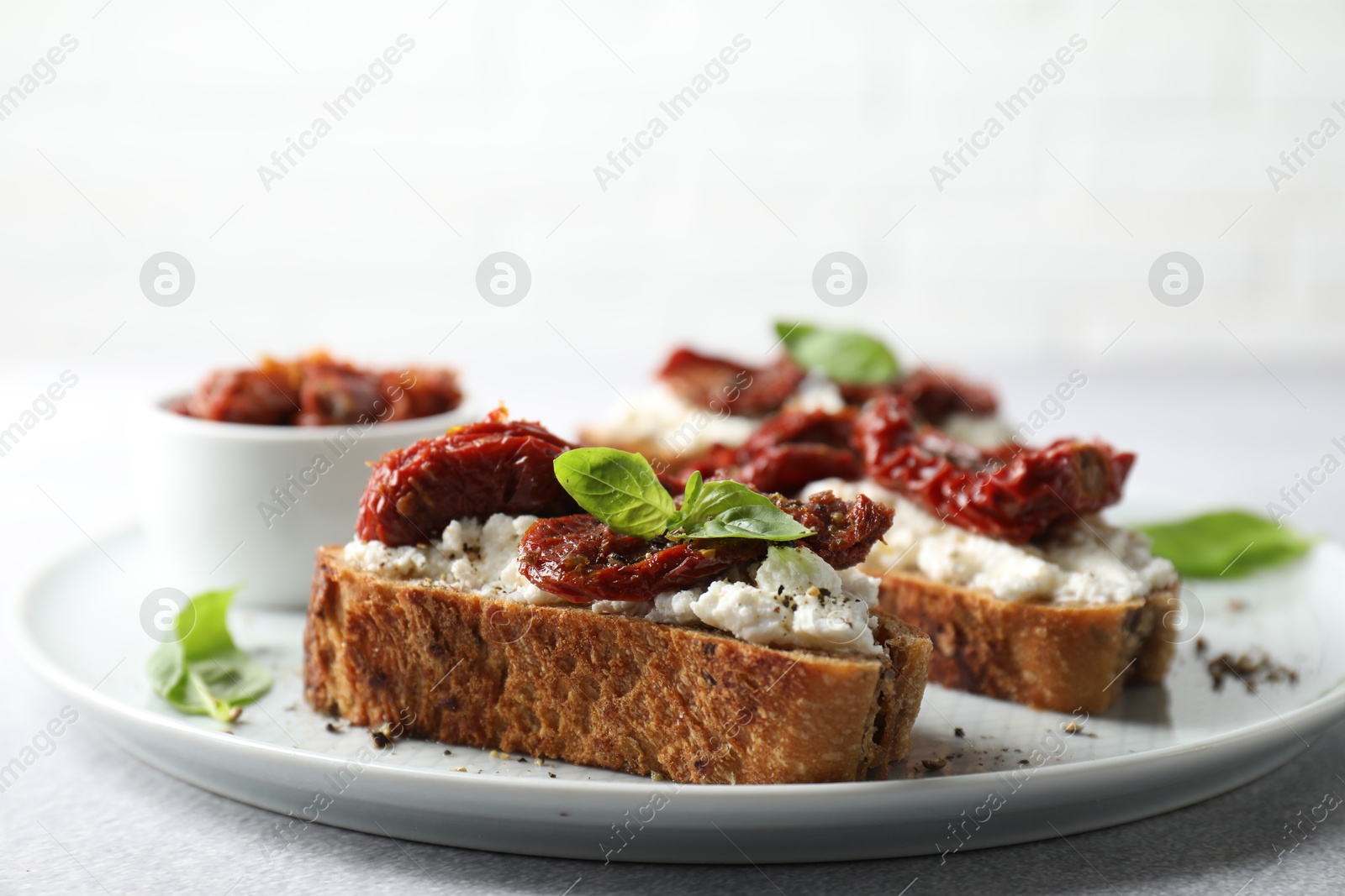 Photo of Delicious ricotta bruschettas with sun dried tomatoes, basil and milled pepper on light table, closeup