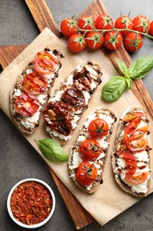 Delicious ricotta bruschettas with sun dried tomatoes, milled chili pepper and basil on grey textured table, flat lay