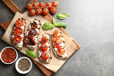 Photo of Delicious ricotta bruschettas with sun dried tomatoes, spices and basil on grey textured table, flat lay. Space for text