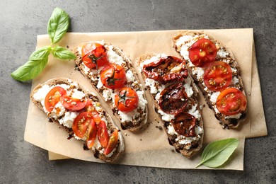 Delicious ricotta bruschettas with sun dried tomatoes, sauce and basil on grey textured table, top view