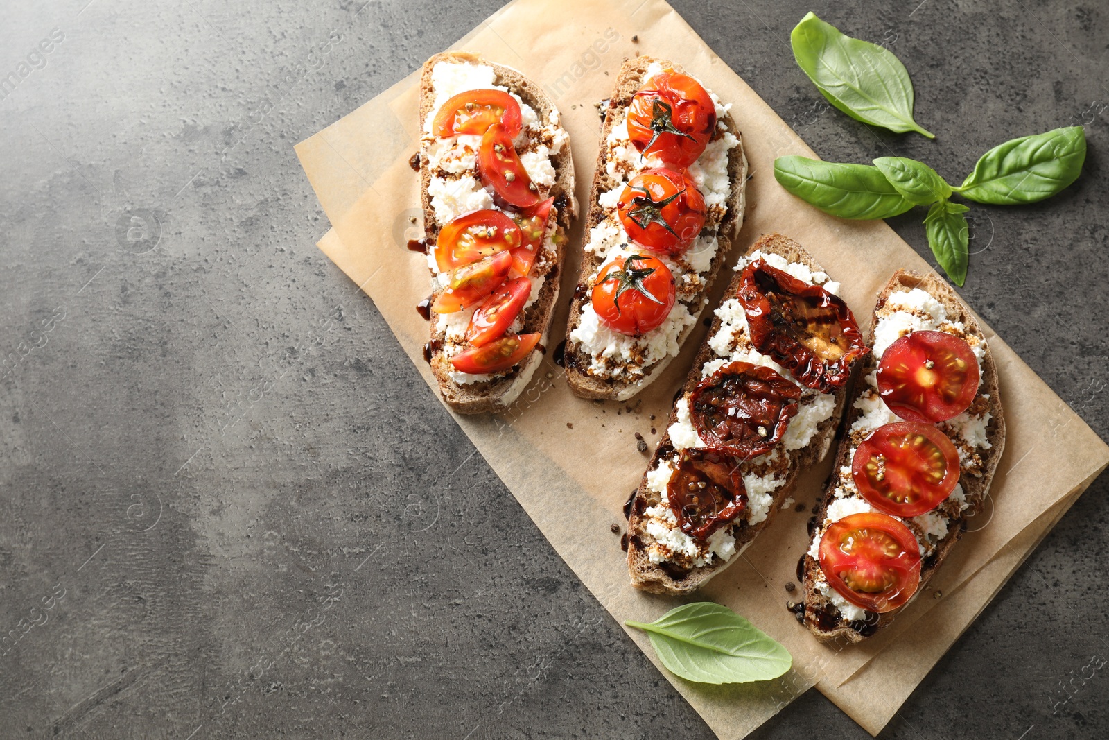 Photo of Delicious ricotta bruschettas with sun dried tomatoes, sauce and basil on grey textured table, top view. Space for text