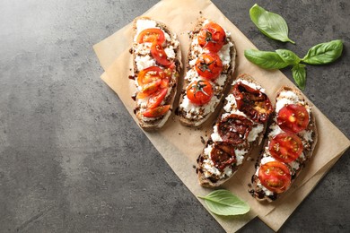 Photo of Delicious ricotta bruschettas with sun dried tomatoes, sauce and basil on grey textured table, top view. Space for text