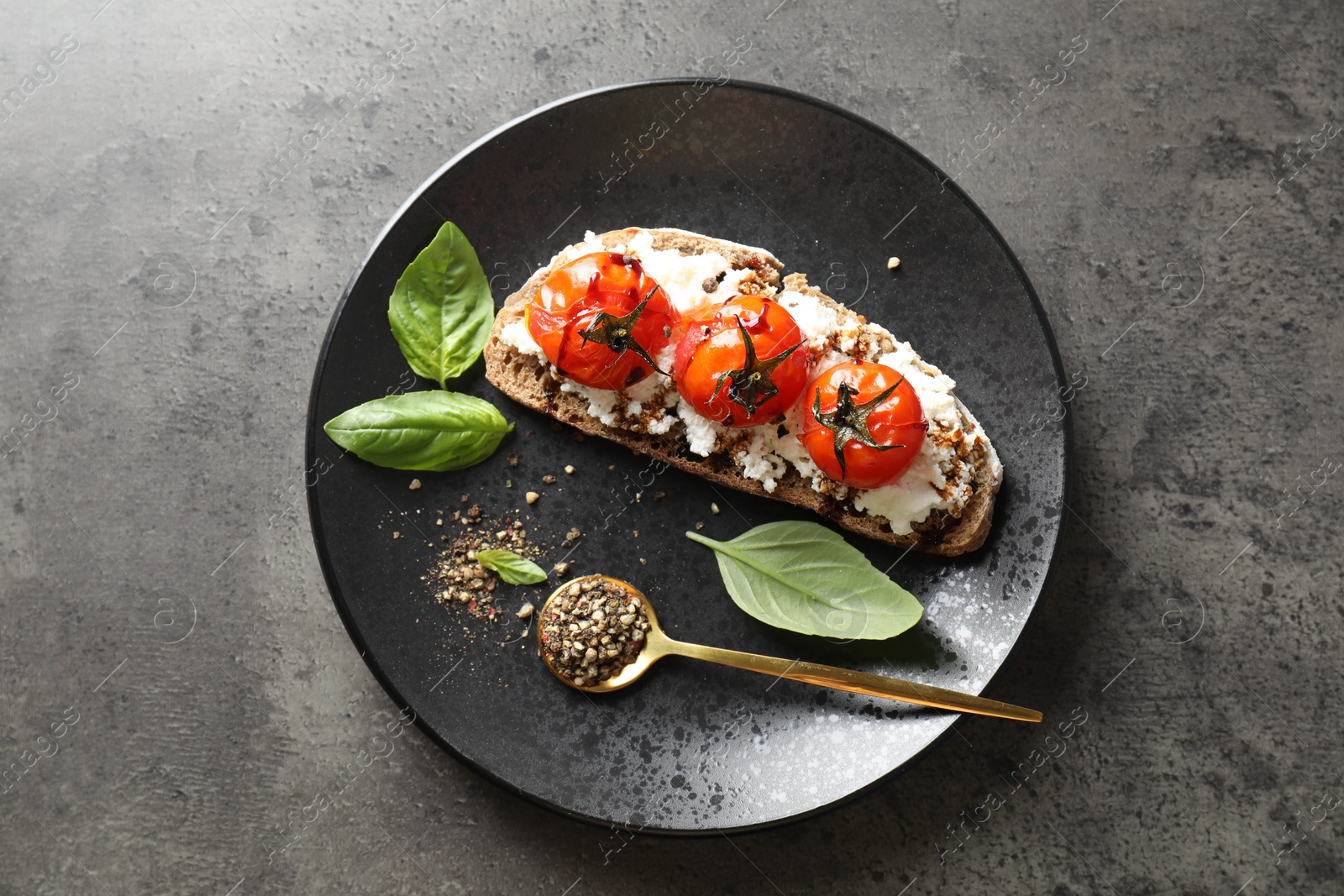 Photo of Delicious ricotta bruschetta with sun dried tomatoes, sauce, basil and milled pepper on grey textured table, top view