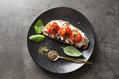 Delicious ricotta bruschetta with sun dried tomatoes, sauce, basil and milled pepper on grey textured table, top view