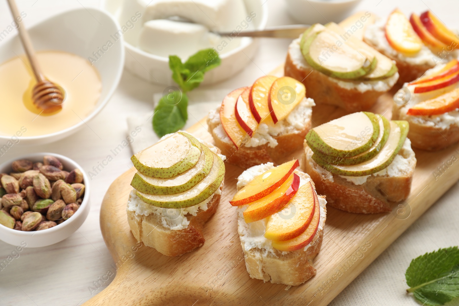 Photo of Delicious ricotta bruschettas with pears, apricots, nuts and mint on white wooden table, closeup