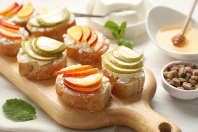 Delicious ricotta bruschettas with pears, apricots, nuts and mint on white wooden table, closeup