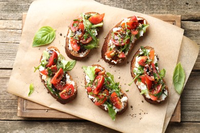 Photo of Delicious ricotta bruschettas with tomatoes, arugula and basil on wooden table, top view