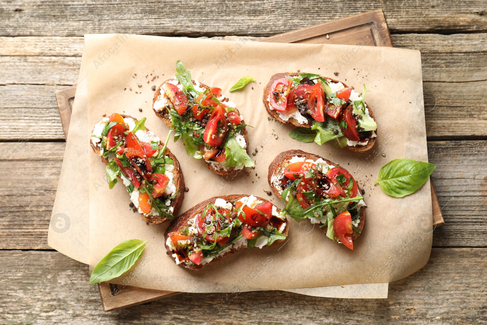 Photo of Delicious ricotta bruschettas with tomatoes, arugula and basil on wooden table, top view