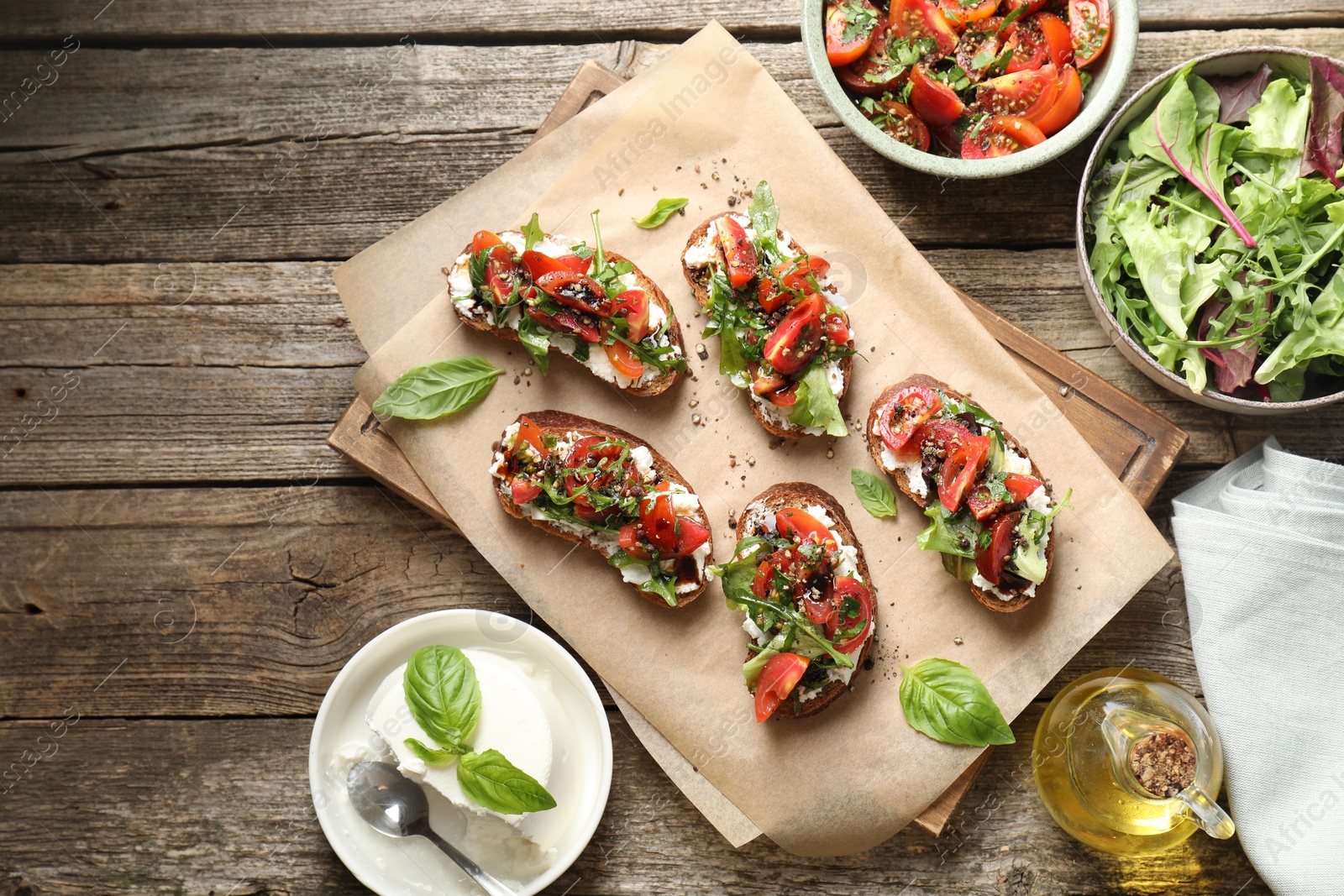 Photo of Delicious ricotta bruschettas with tomatoes, arugula and basil on wooden table, flat lay