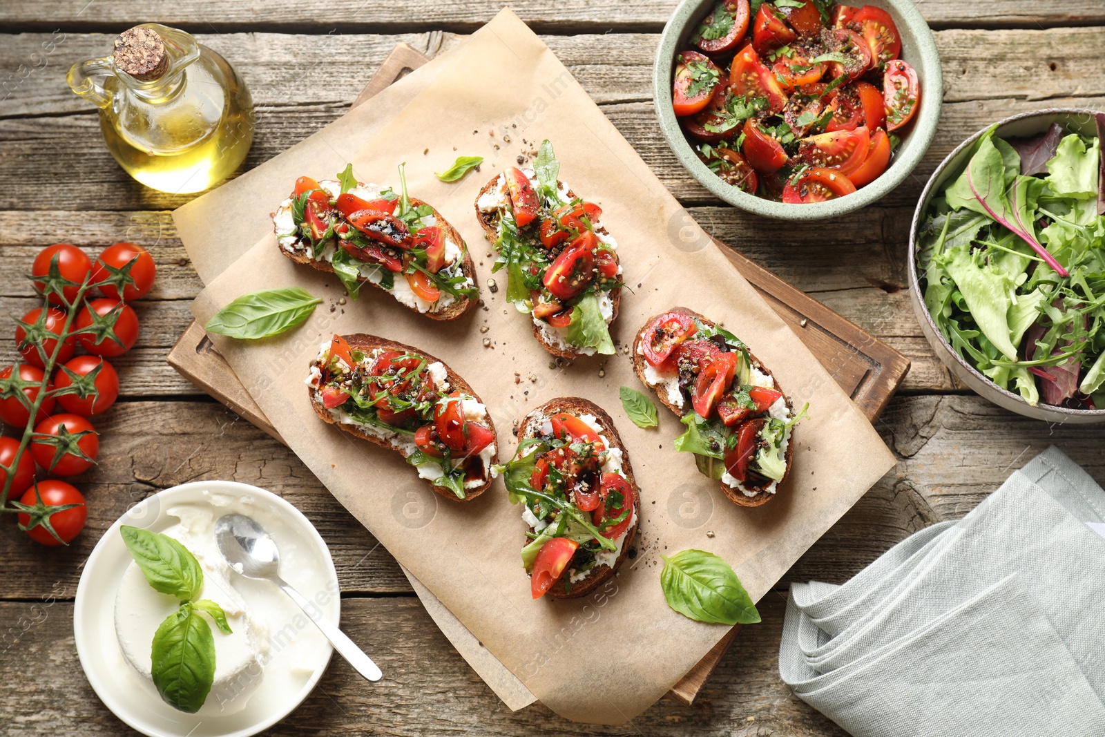 Photo of Delicious ricotta bruschettas with tomatoes, arugula and basil on wooden table, flat lay