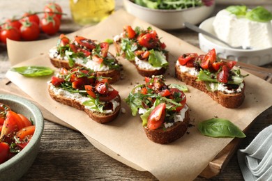 Photo of Delicious ricotta bruschettas with tomatoes, arugula and basil on wooden table, closeup