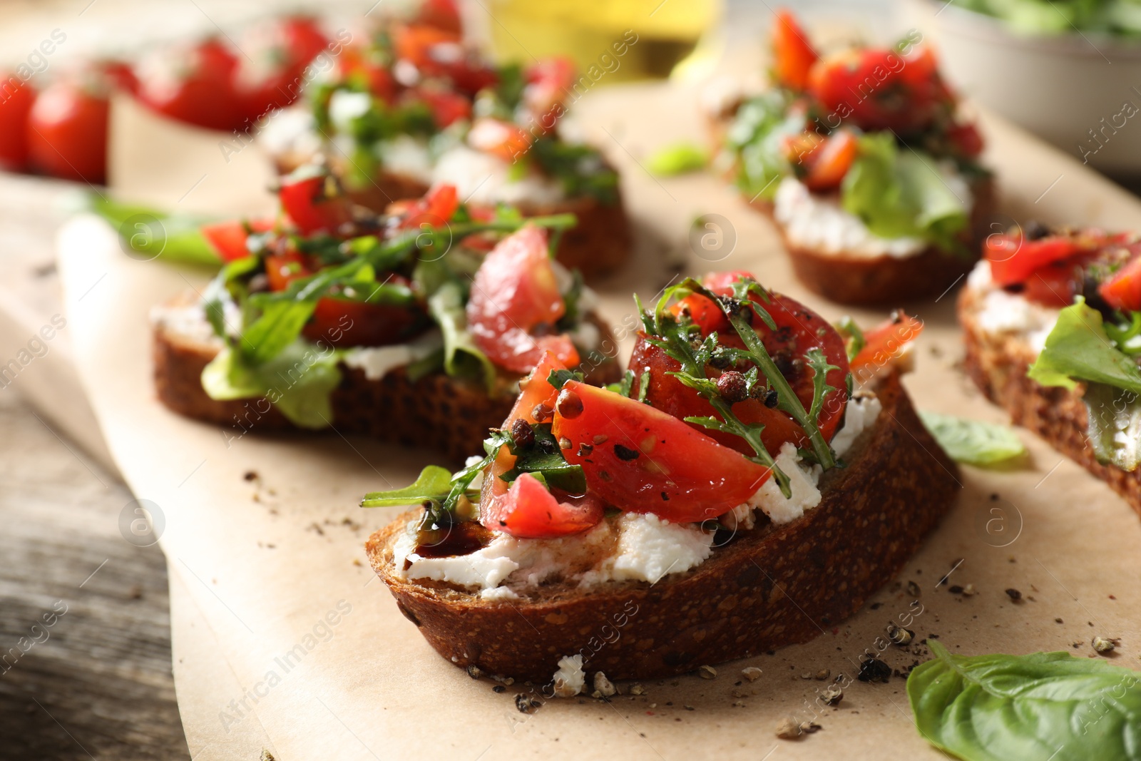 Photo of Delicious ricotta bruschettas with tomatoes, arugula and basil on wooden table, closeup