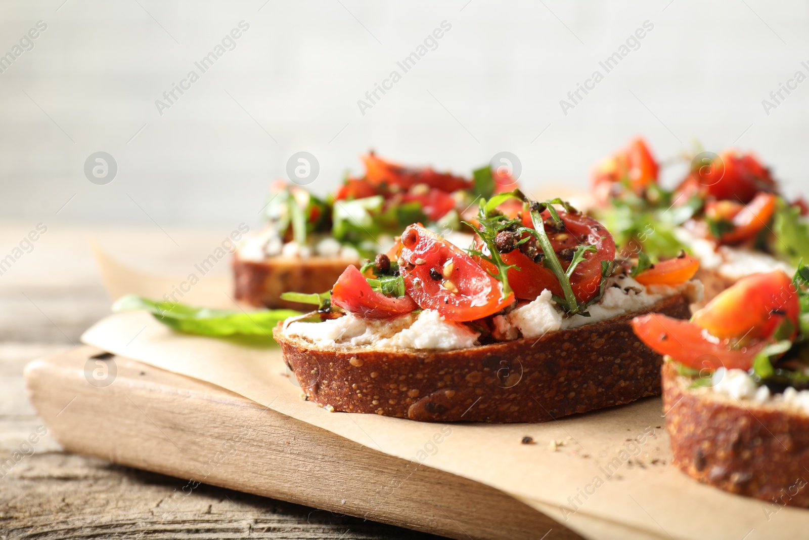 Photo of Delicious ricotta bruschettas with tomatoes and arugula on wooden table, closeup