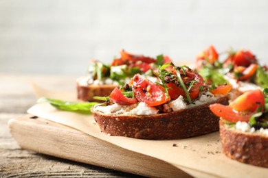 Delicious ricotta bruschettas with tomatoes and arugula on wooden table, closeup