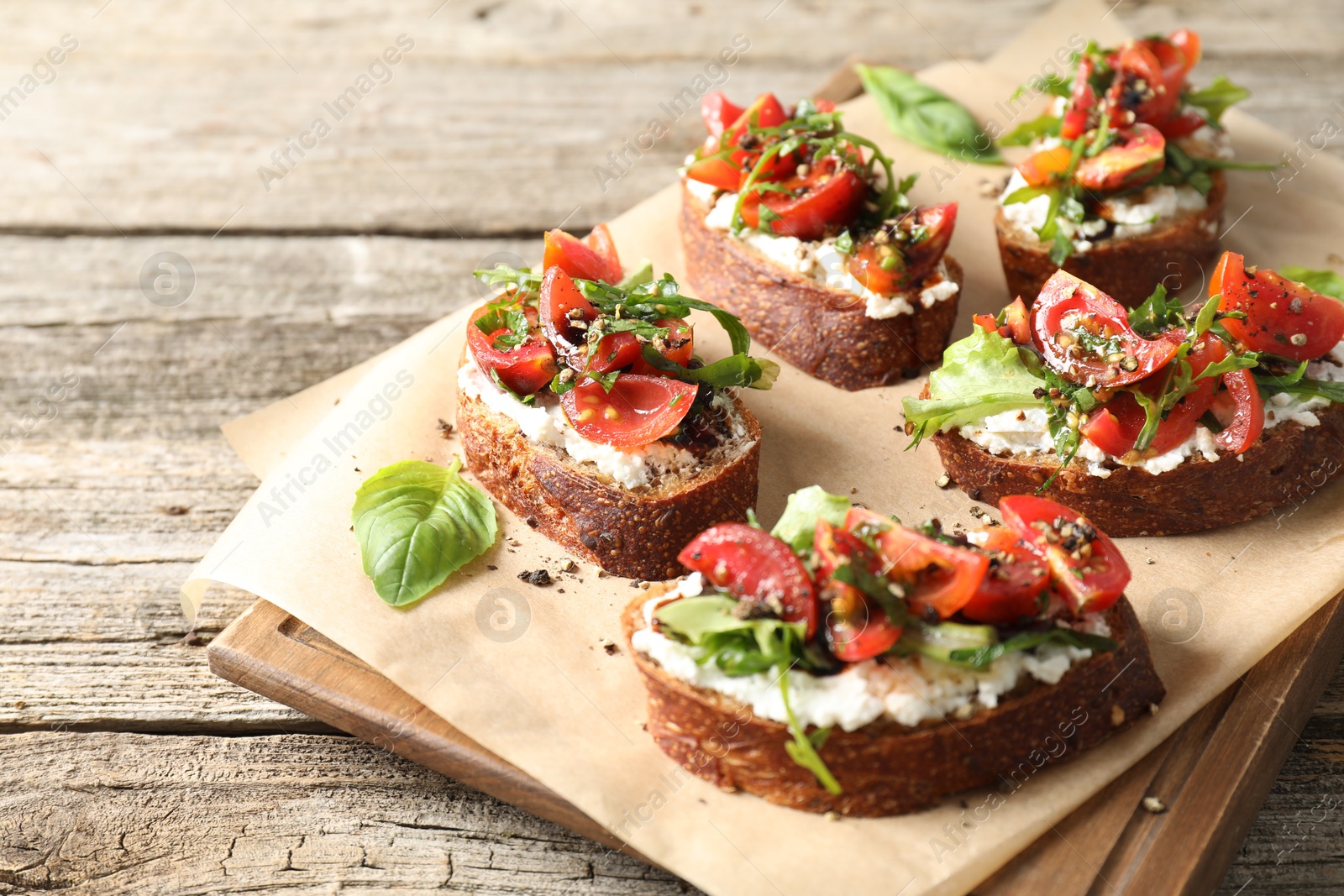 Photo of Delicious ricotta bruschettas with tomatoes, arugula and basil on wooden table, closeup