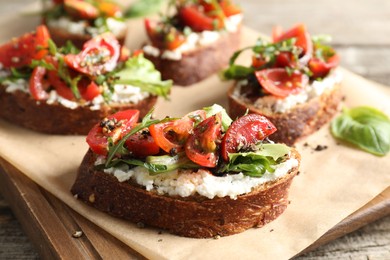 Photo of Delicious ricotta bruschettas with tomatoes and arugula on wooden table, closeup