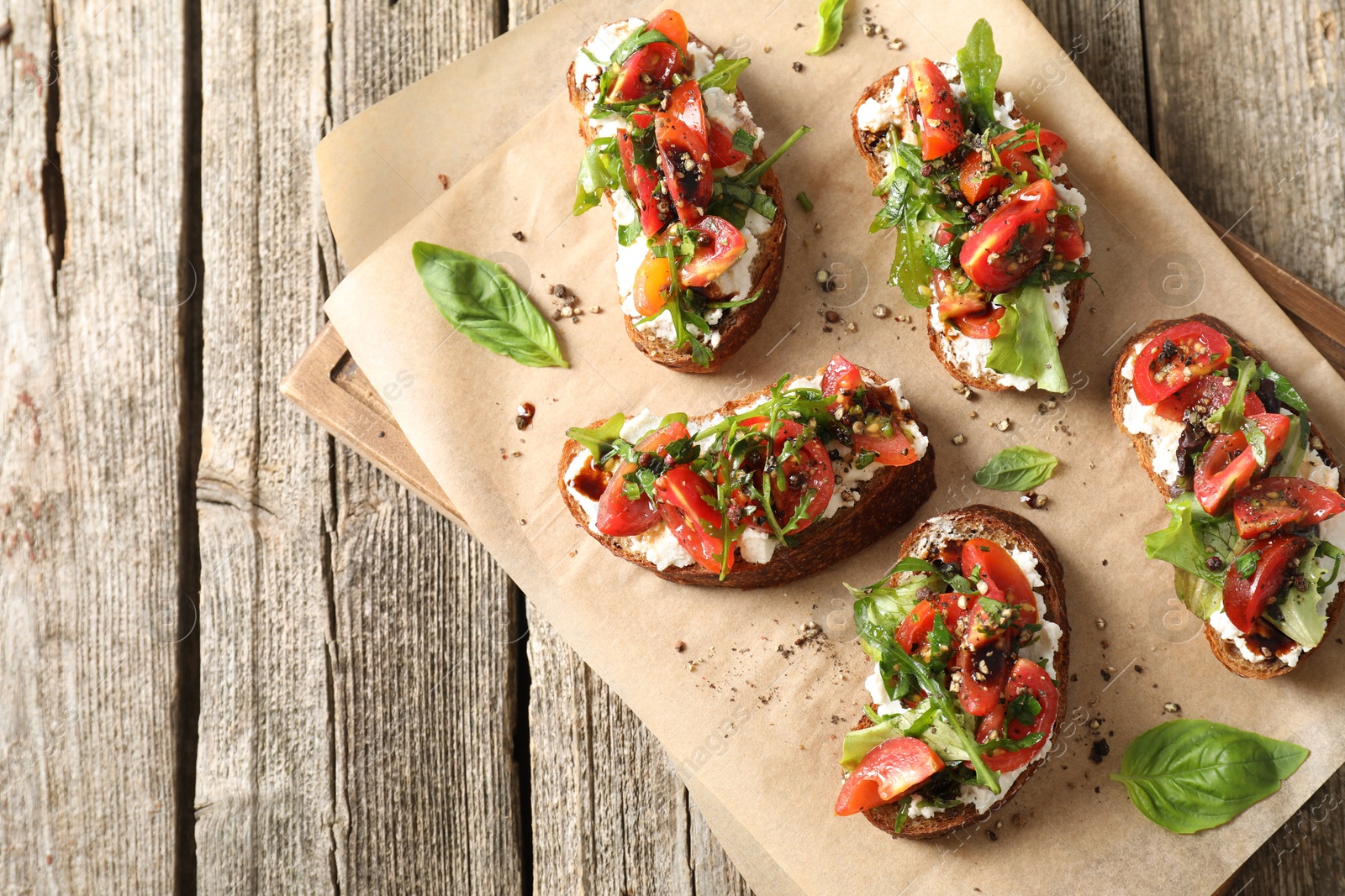 Photo of Delicious ricotta bruschettas with tomatoes, arugula and basil on wooden table, top view. Space for text