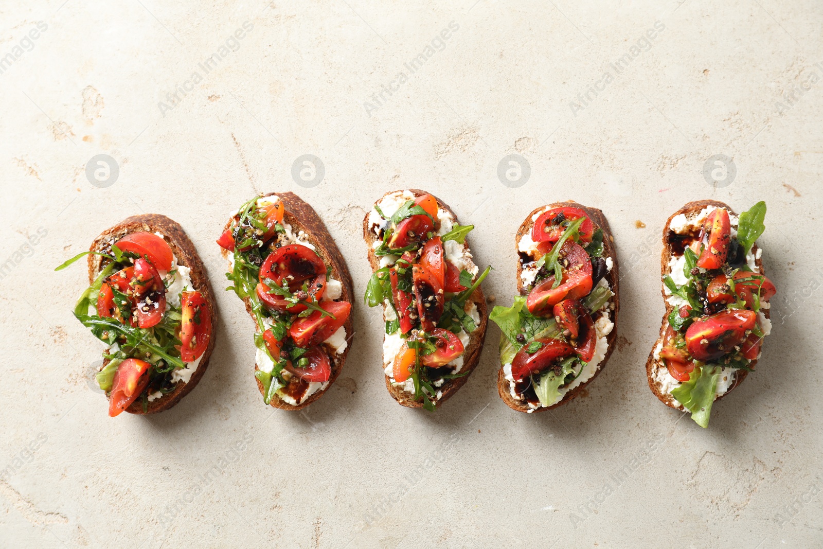 Photo of Delicious bruschettas with ricotta cheese, tomatoes and arugula on light textured table, flat lay