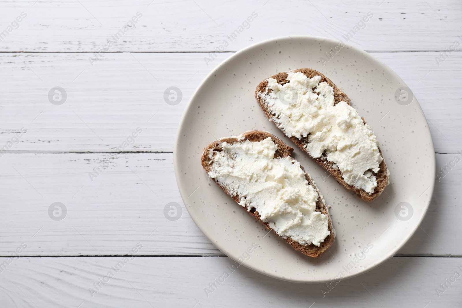 Photo of Bruschettas with ricotta cheese on white wooden table, top view. Space for text