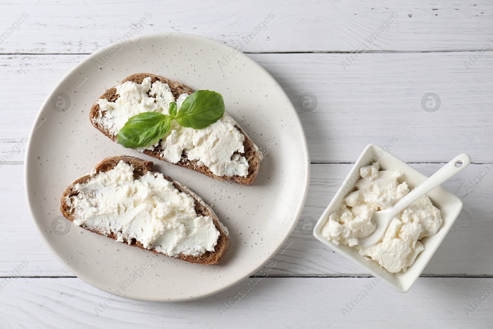 Photo of Bruschettas with ricotta cheese and basil on white wooden table, top view