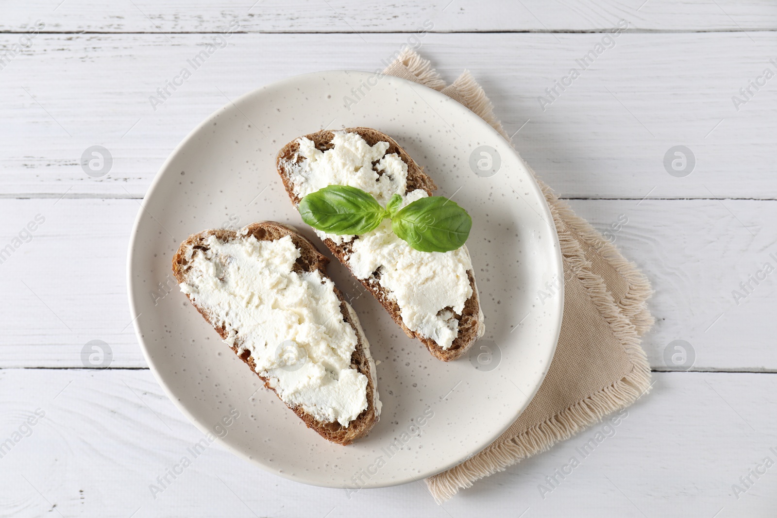 Photo of Bruschettas with ricotta cheese and basil on white wooden table, top view