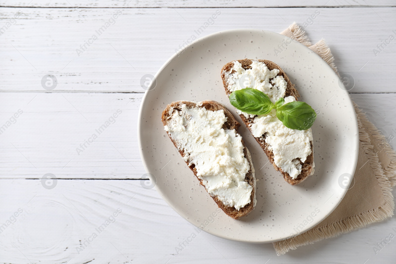 Photo of Bruschettas with ricotta cheese and basil on white wooden table, top view. Space for text