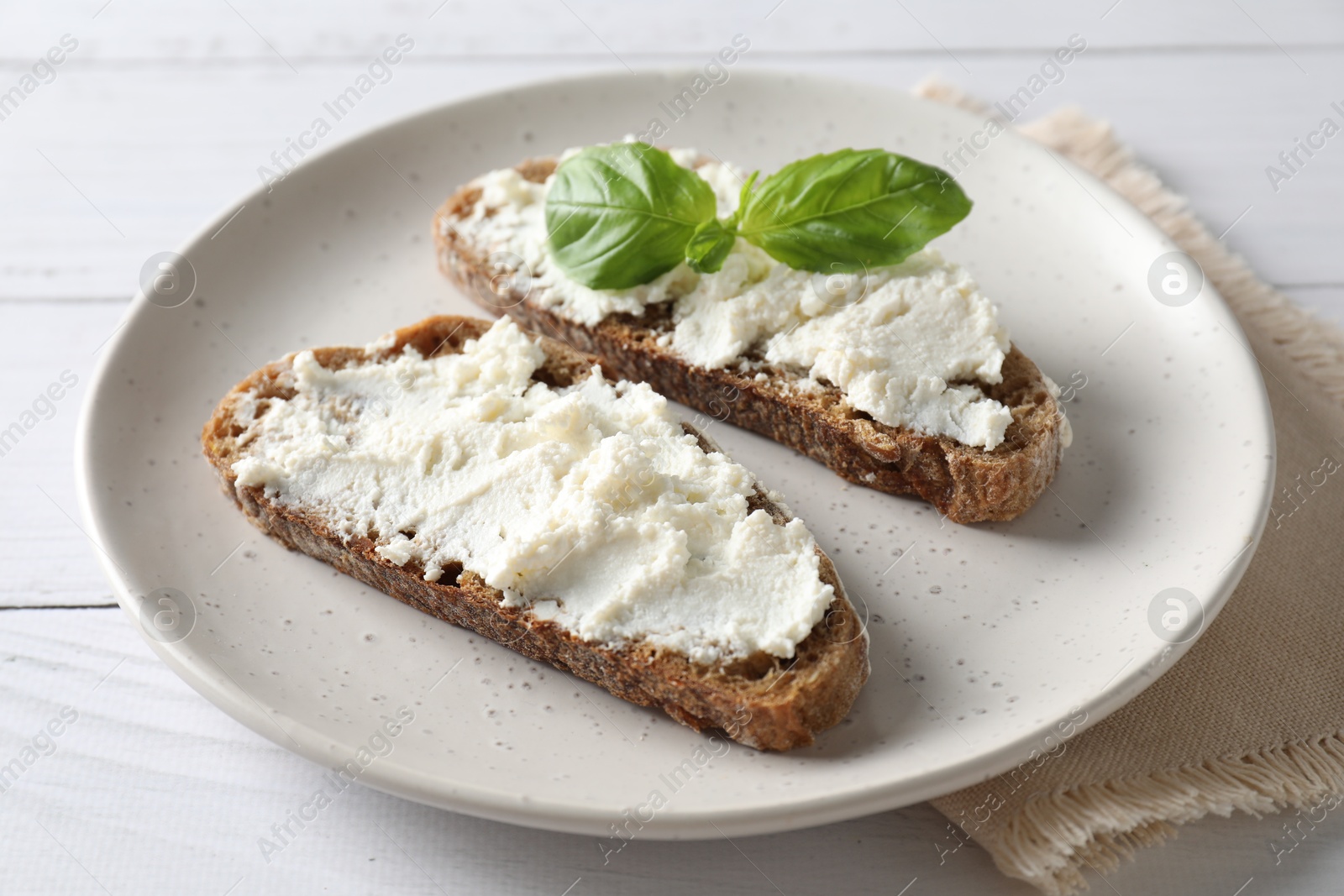 Photo of Bruschettas with ricotta cheese and basil on white wooden table, closeup