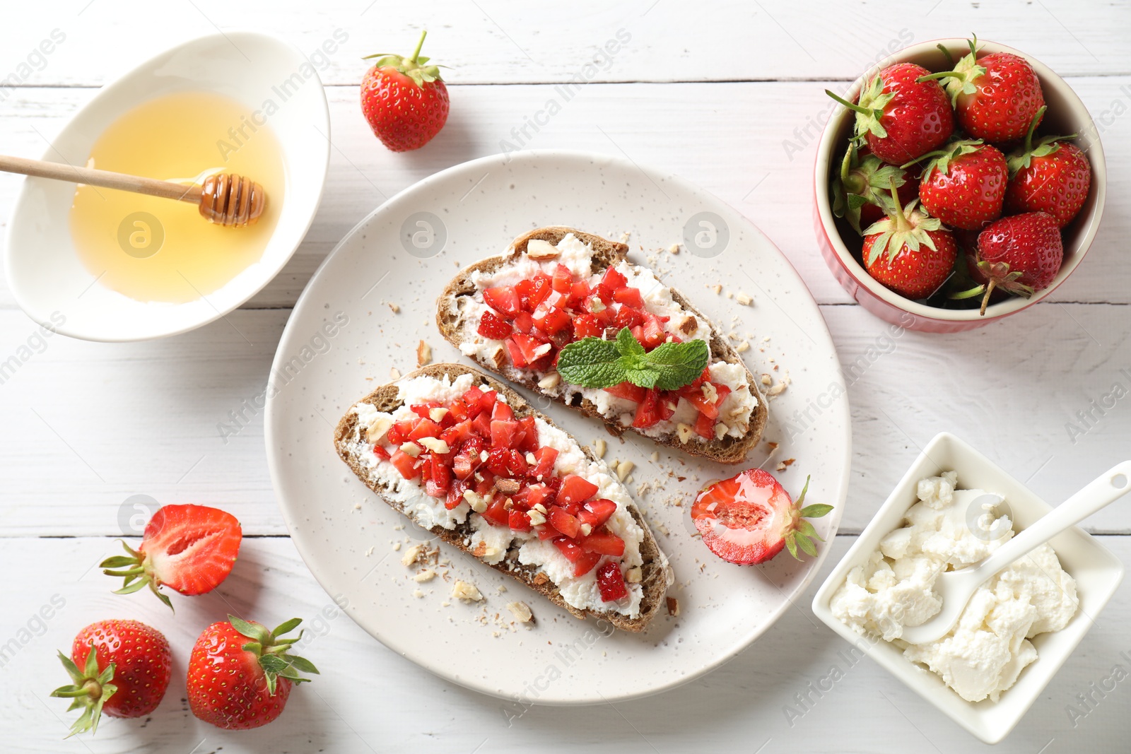 Photo of Bruschettas with ricotta cheese, chopped strawberries and mint on white wooden table, flat lay