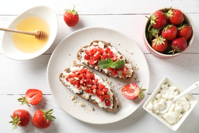 Bruschettas with ricotta cheese, chopped strawberries and mint on white wooden table, flat lay