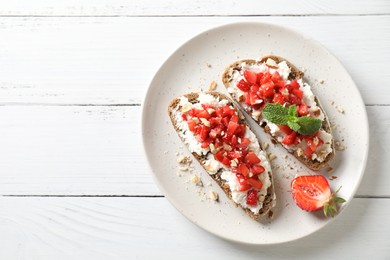 Photo of Bruschettas with ricotta cheese, chopped strawberries and mint on white wooden table, top view. Space for text