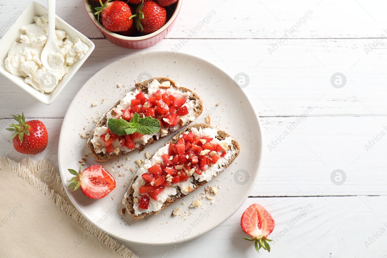 Photo of Bruschettas with ricotta cheese, chopped strawberries and mint on white wooden table, flat lay. Space for text