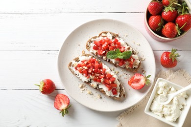 Photo of Bruschettas with ricotta cheese, chopped strawberries and mint on white wooden table, flat lay