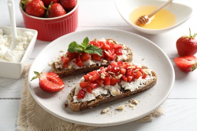 Photo of Bruschettas with ricotta cheese, chopped strawberries and mint on white wooden table, closeup