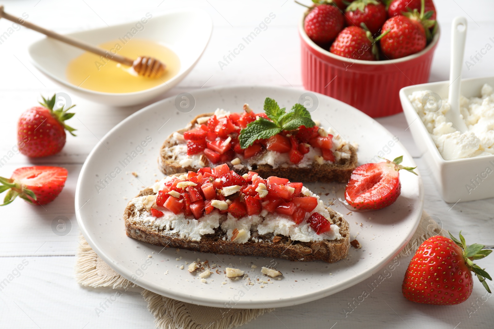 Photo of Bruschettas with ricotta cheese, chopped strawberries and mint on white wooden table, closeup