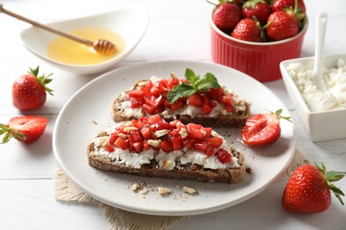 Bruschettas with ricotta cheese, chopped strawberries and mint on white wooden table, closeup