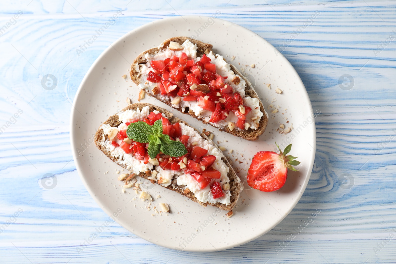 Photo of Bruschettas with ricotta cheese, chopped strawberries and mint on blue wooden table, top view