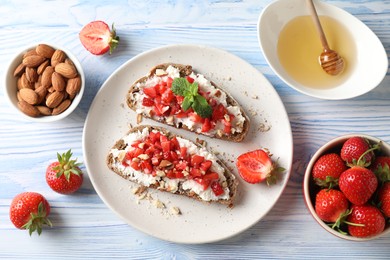 Bruschettas with ricotta cheese, chopped strawberries and mint on blue wooden table, flat lay