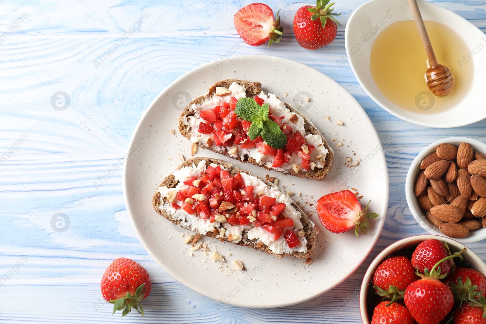 Photo of Bruschettas with ricotta cheese, chopped strawberries and mint on blue wooden table, flat lay