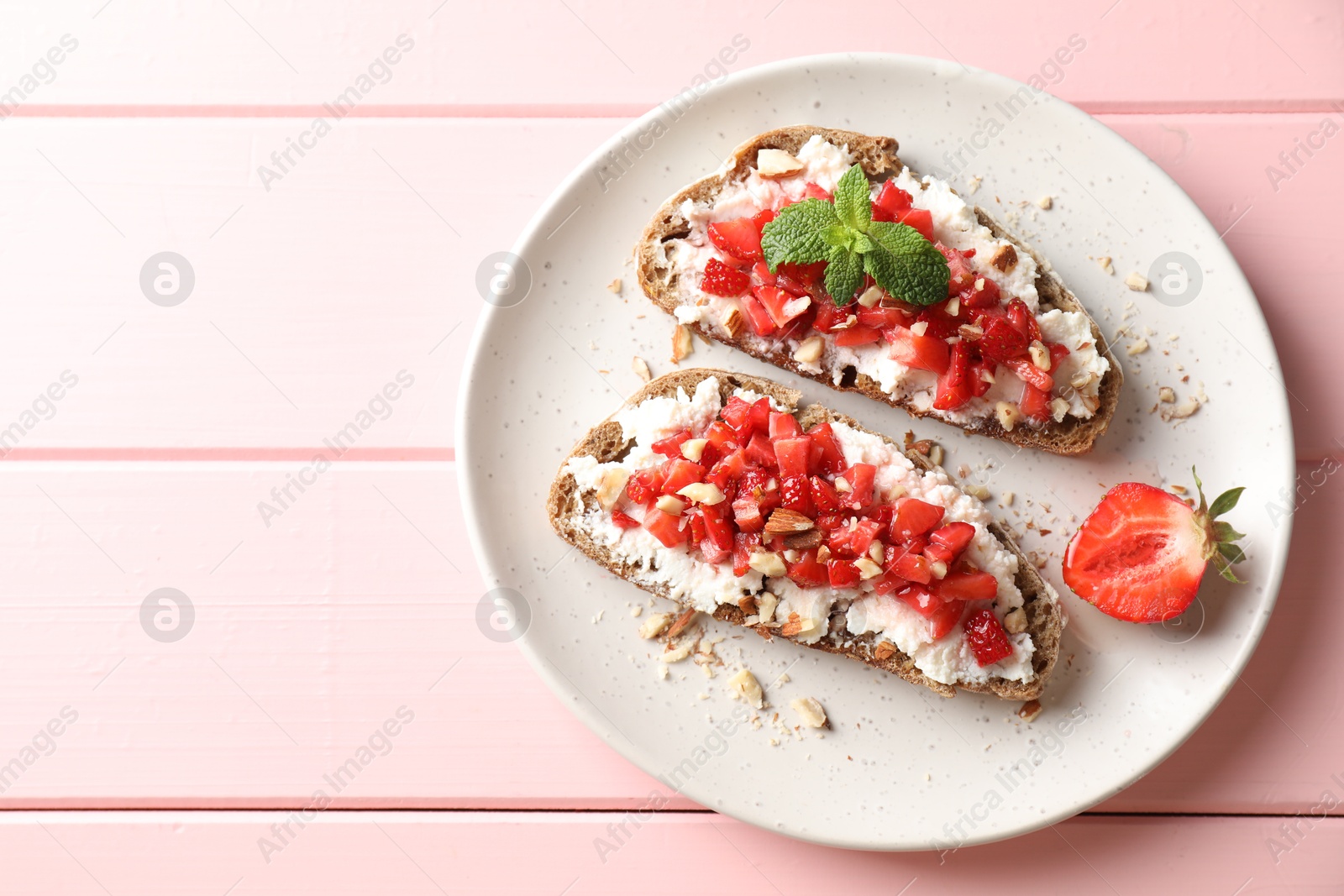 Photo of Bruschettas with ricotta cheese, chopped strawberries and mint on pink wooden table, top view