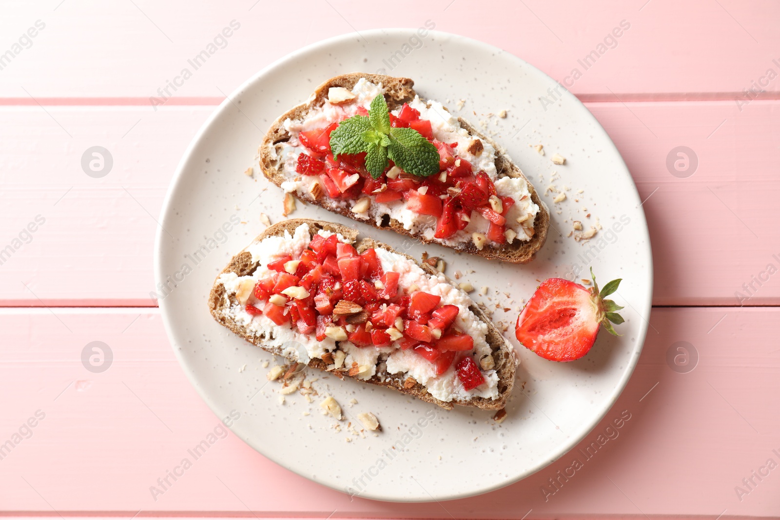 Photo of Bruschettas with ricotta cheese, chopped strawberries and mint on pink wooden table, top view