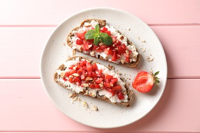 Bruschettas with ricotta cheese, chopped strawberries and mint on pink wooden table, top view