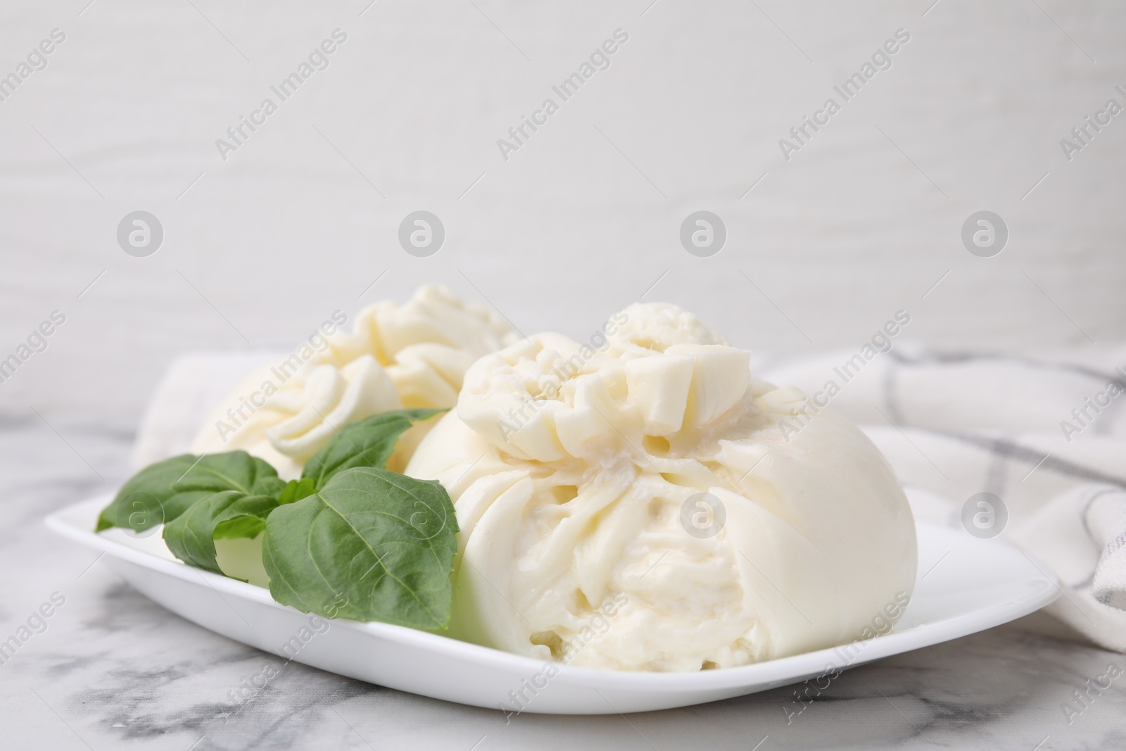 Photo of Delicious burrata cheese and basil on white marble table, closeup