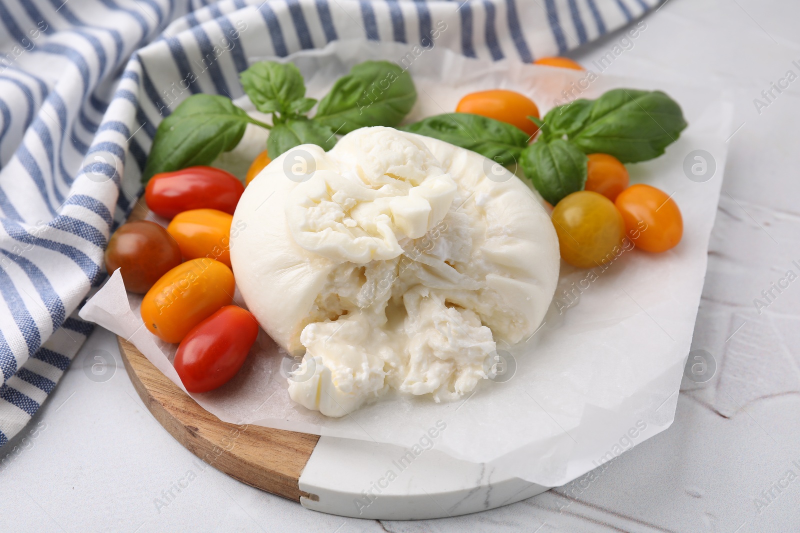 Photo of Delicious fresh burrata cheese with basil leaves and tomatoes on white textured table