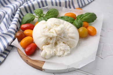 Delicious fresh burrata cheese with basil leaves and tomatoes on white textured table