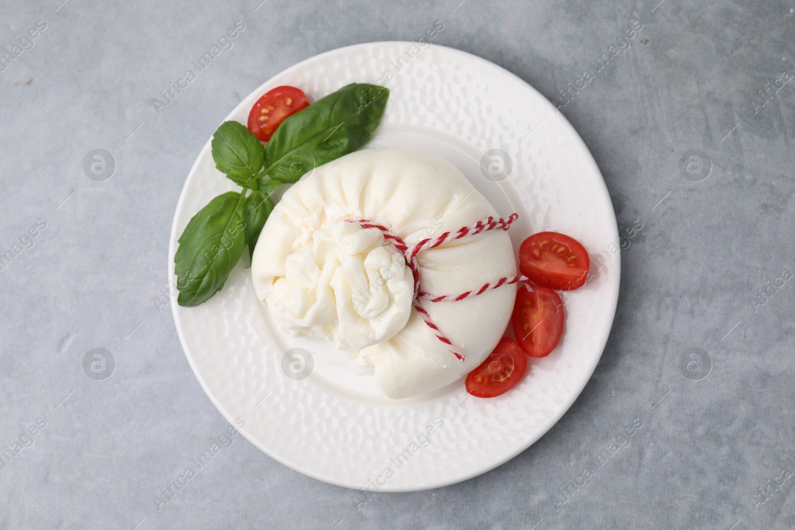 Photo of Delicious fresh burrata cheese with basil leaves and tomato on grey table, top view