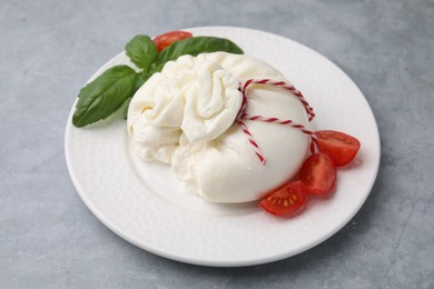 Photo of Delicious fresh burrata cheese with basil leaves and tomato on grey table