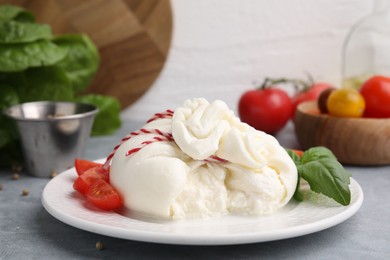 Photo of Delicious fresh burrata cheese with basil leaves and tomato on grey table