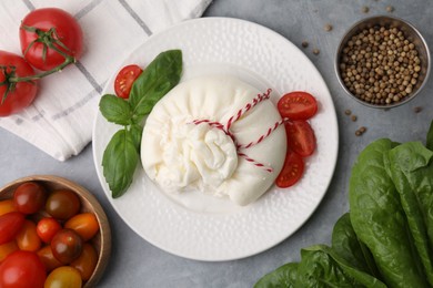 Photo of Delicious fresh burrata cheese with tomatoes and spices on grey table, flat lay